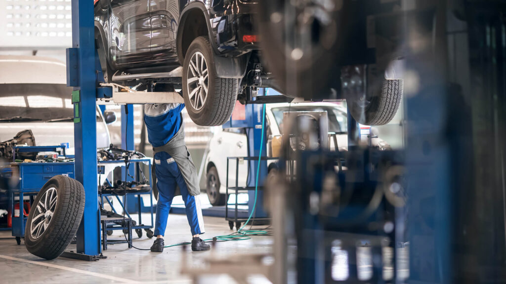 Mechanic inspecting car suspension detail and wheel car of lifted automobile at repair service station. Tire service station. Preventive maintenance.